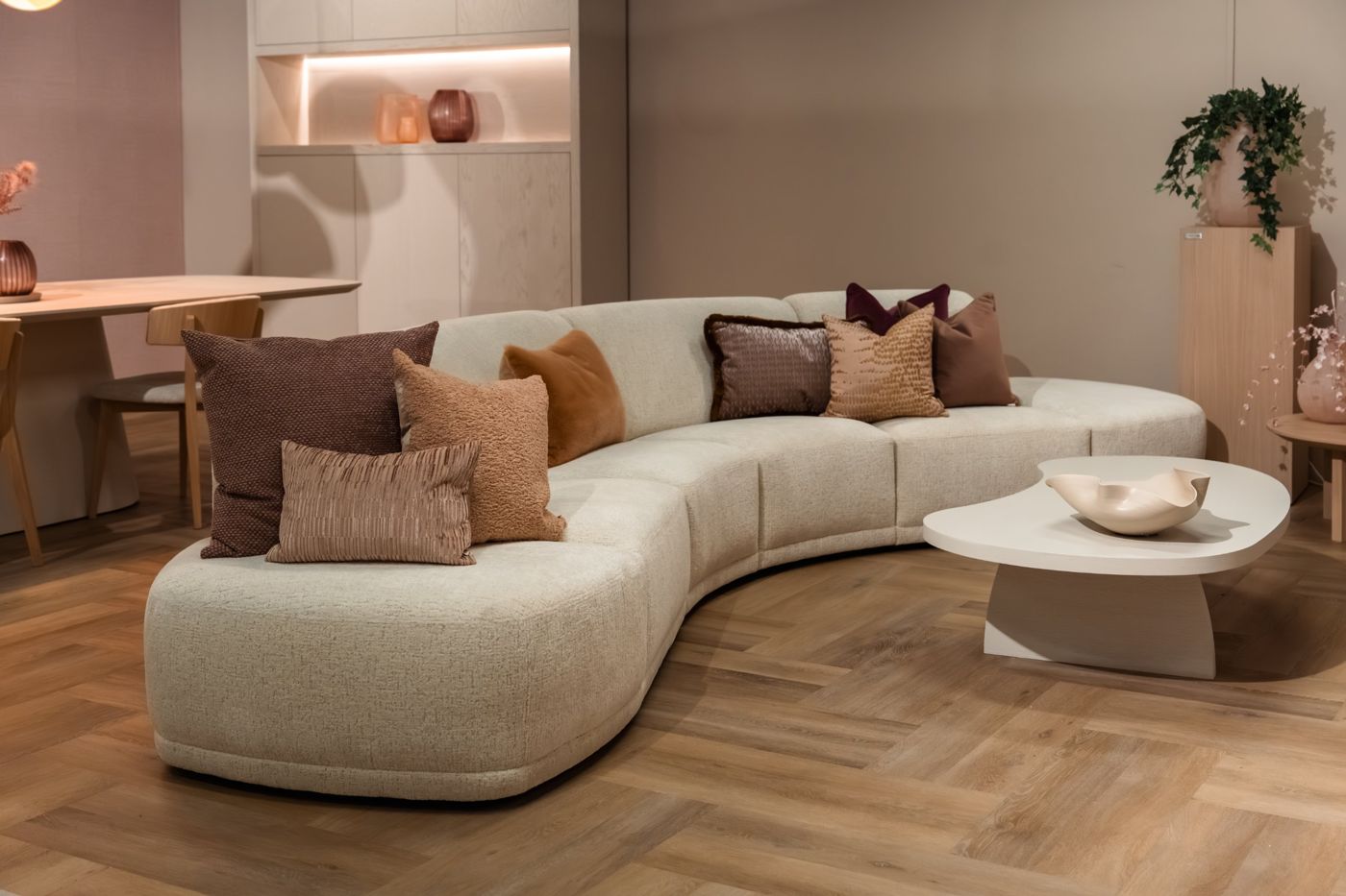 Ronde hoeksofa in lichte bouclé met kussens in warme tinten en een organische salontafel