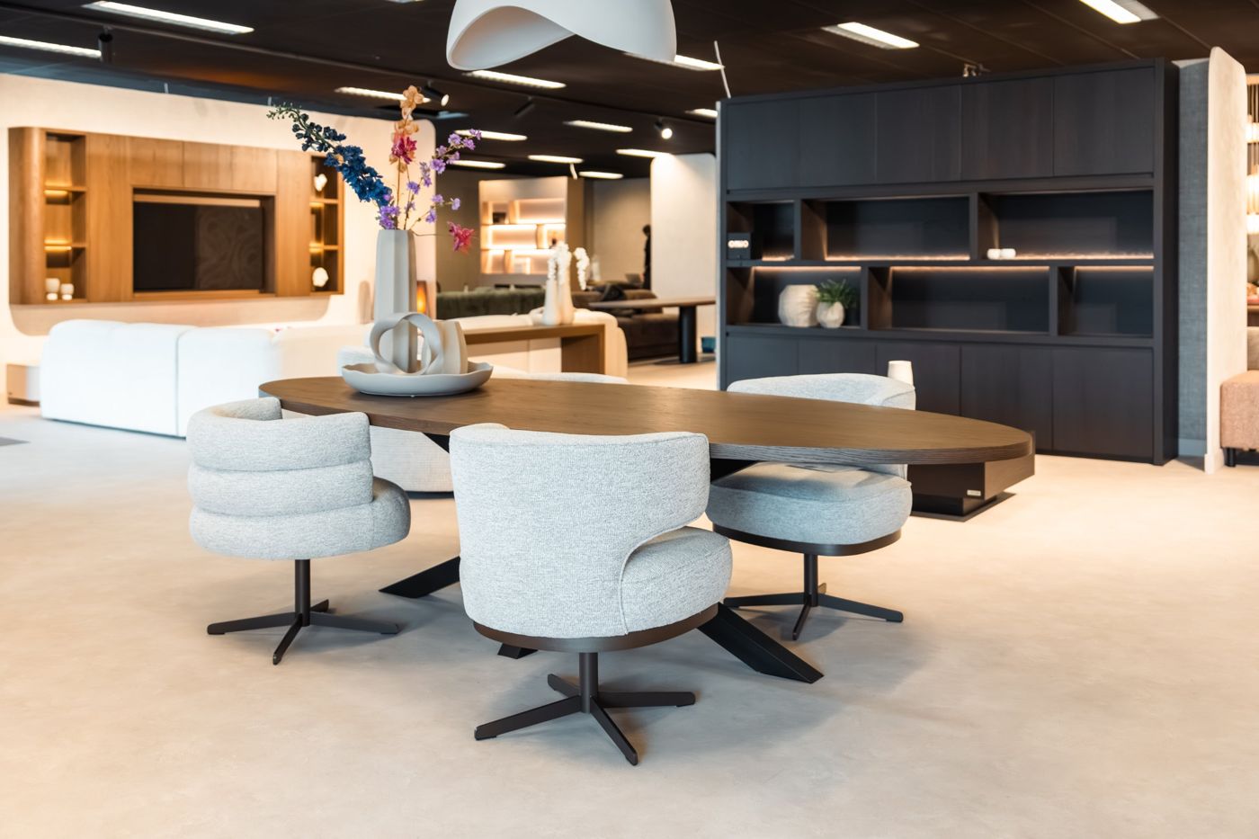 Ovale donkere eettafel met lichtgrijze draaibare eetkamerstoelen in de showroom